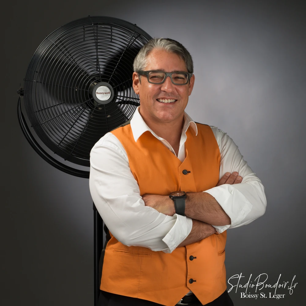 photo de base d'un chef d'entreprise Portrait dynamique d'un entrepreneur à lunettes en gilet orange avec ventilateur studio en arrière-plan, photographe corporate Val-de-Marne.
