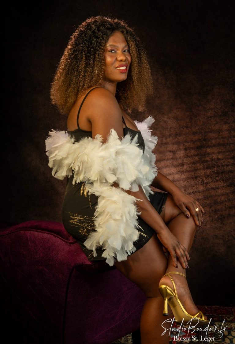 Les Antilles au Studio Boudoir Portrait boudoir d'une femme antillaise à la peau noire souriante avec boa en plumes blanches au studio de Boissy-Saint-Léger